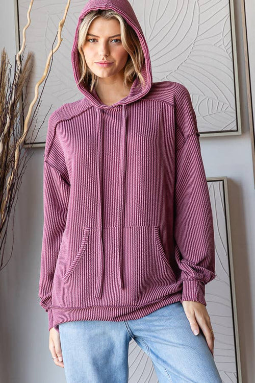 Woman wearing a ribbed pink hoodie and light blue jeans indoors.