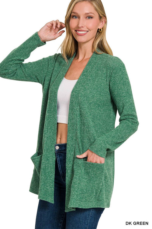 A woman modeling a heathered green open-front cardigan with long sleeves and front pockets, worn over a white crop top and blue jeans against a plain white background.