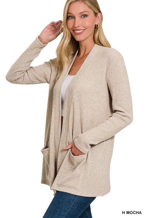 A woman modeling a long-sleeve, open-front ribbed cardigan in a warm beige or mocha shade, worn over a white top and blue jeans against a plain white background.