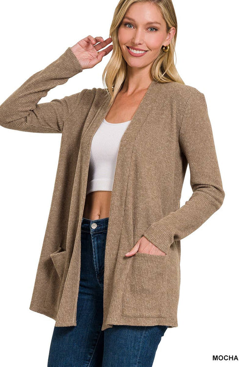 A woman modeling a long-sleeve, open-front cardigan in a warm taupe or mocha brown color, worn over a white crop top and blue jeans against a plain white background.