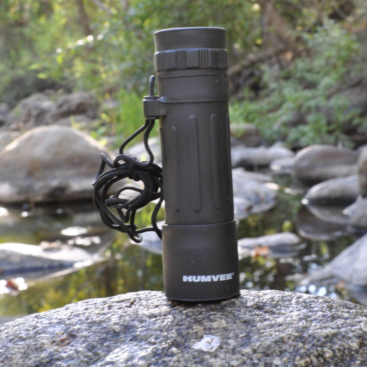 Black monocular with 'HUMVEE' branding on a rock by a water body