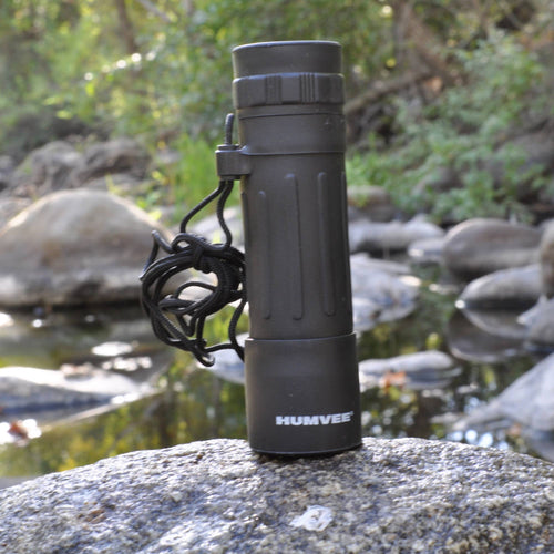 Black monocular with 'HUMVEE' branding on a rock by a water body