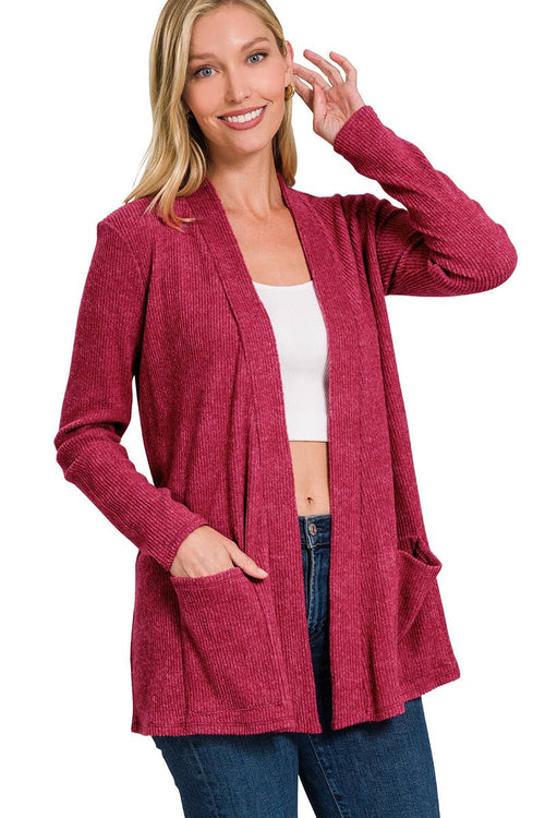 A woman wearing a heathered magenta open-front cardigan with pockets over a white crop top and blue jeans, photographed against a plain white background.