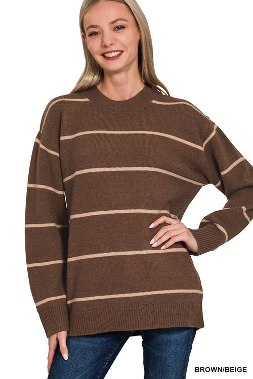 A woman wearing a brown knit sweater with horizontal beige stripes, paired with blue jeans, against a plain white background.