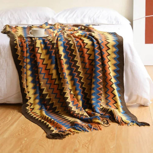 Colorful zigzag patterned blanket draped over a bed with a wooden floor.