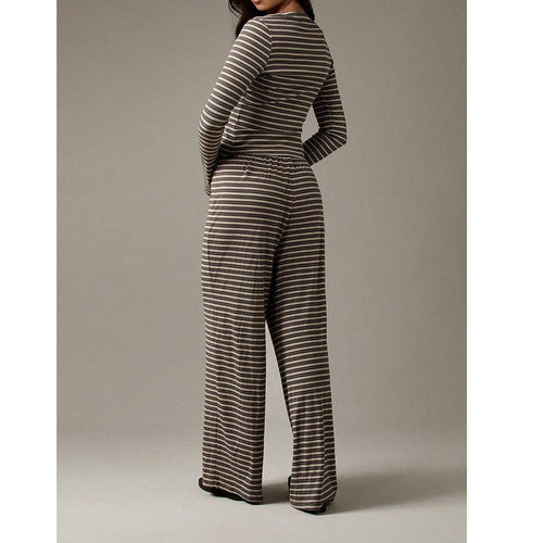 A woman shown from the back wearing a long-sleeve knit jumpsuit with thin horizontal brown and beige stripes, photographed against a plain warm gray studio background.
