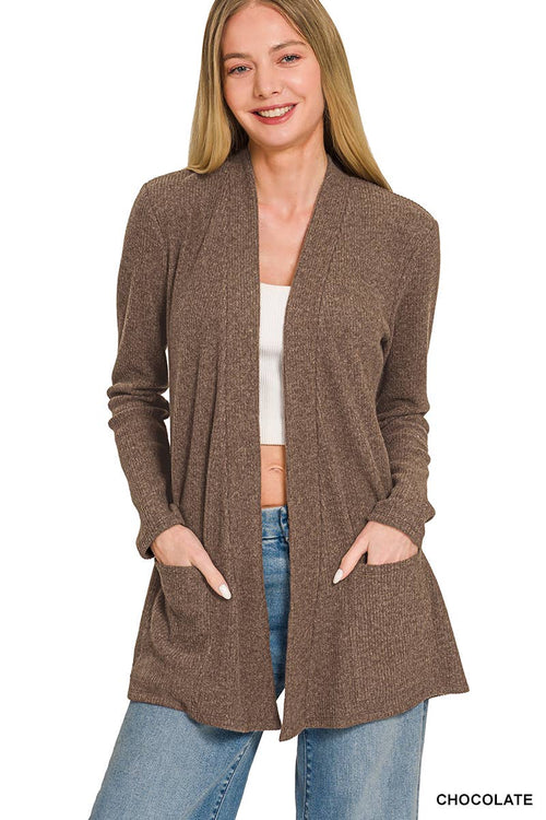 A woman modeling a brown open-front cardigan with long sleeves, front pockets, and a relaxed fit, paired with a white top and blue jeans against a plain white background.