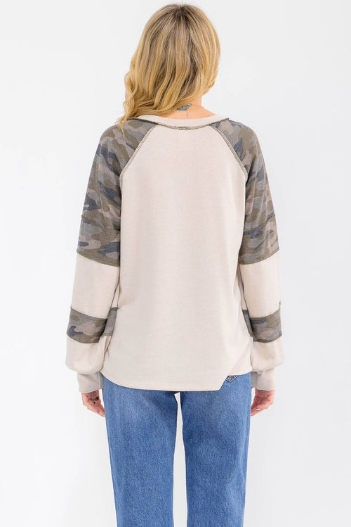 Woman wearing a camouflage and beige long-sleeve shirt with blue jeans on a white background