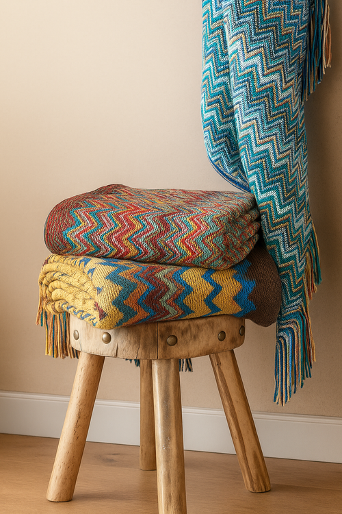 Wooden stool with colorful patterned Blankets and a blanket draped over it against a beige wall.
