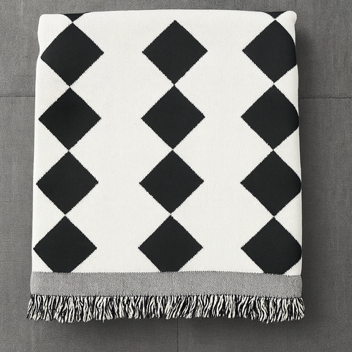 A folded throw blanket with a black and white diamond argyle pattern and fringed edges, laid flat on a dark gray textured surface.