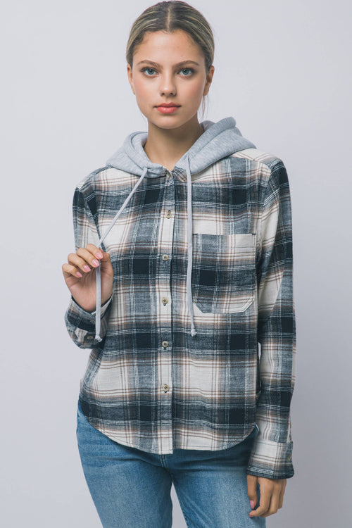 A woman modeling a hooded button-up shirt with a blue, gray, and white plaid pattern, featuring a light gray hood and drawstrings, paired with blue jeans against a plain gray studio background.