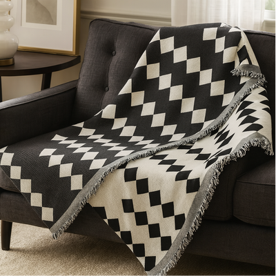 A black and off-white diamond-patterned throw blanket with fringed edges draped over a dark gray armchair in a living room setting.