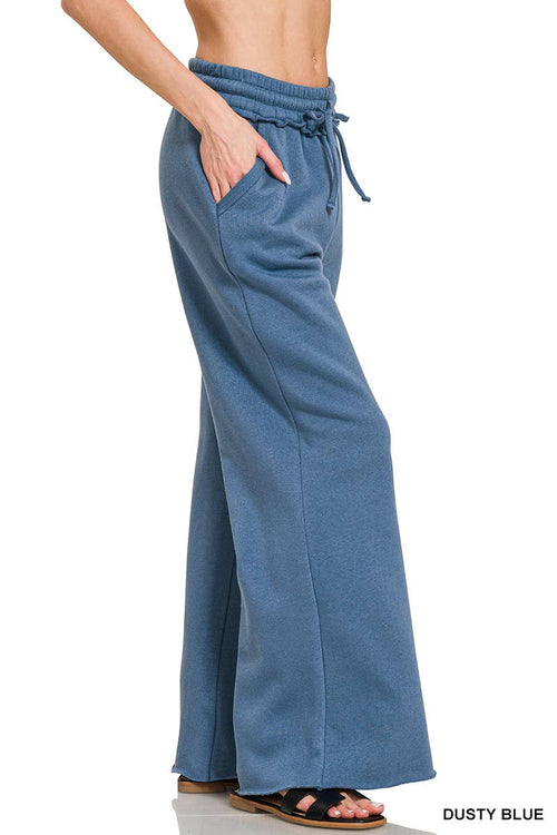 A person wearing dusty blue wide-leg sweatpants with a drawstring waistband, shown from the waist down against a white background.