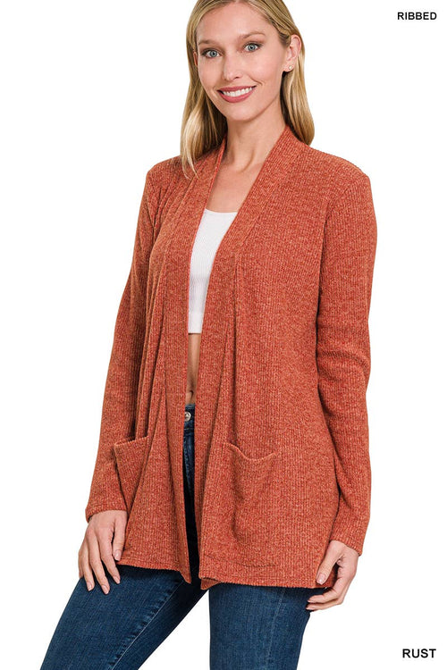 A woman modeling a rust-colored ribbed open-front cardigan with large front patch pockets, worn over a white top and blue jeans against a plain white background.