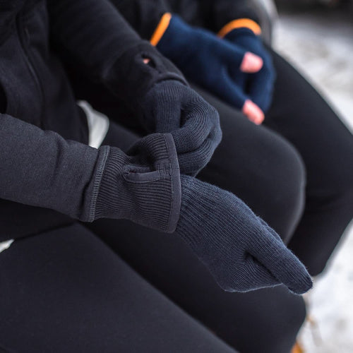 Close-up of dark gray gloves held by a person wearing black pants.