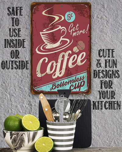 A decorative rectangular metal sign with a distressed coffee-themed design hangs on a gray wall above a kitchen utensil holder. The sign is reddish brown with cream lettering reading 'Coffee' and 'Get more!', plus a cup illustration and small coffee beans.