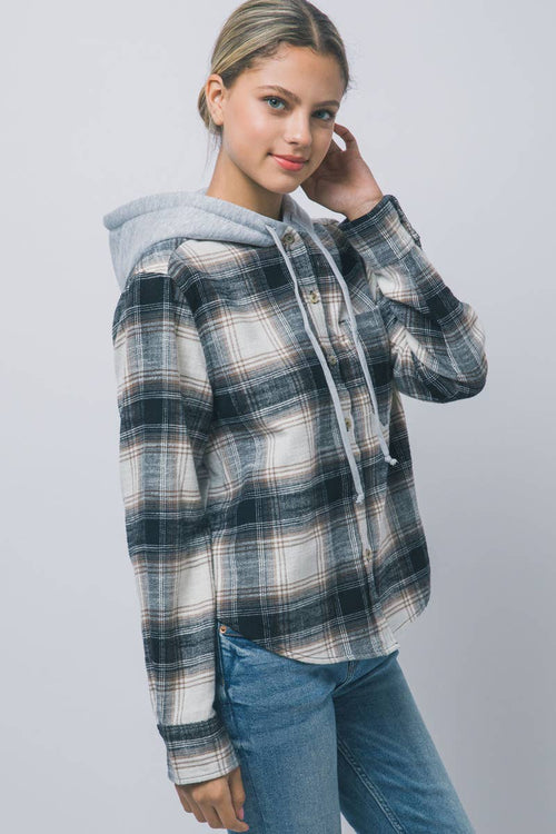 A woman modeling a plaid hooded button-up shirt with a light gray hood, paired with blue jeans, against a plain light gray studio background.