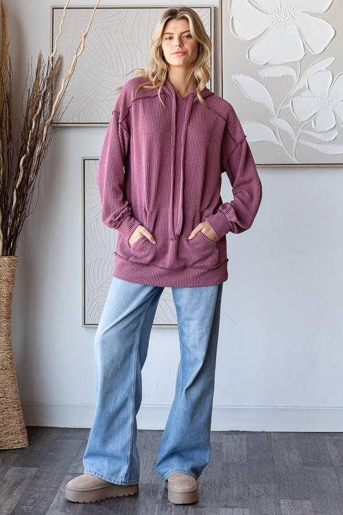 Woman wearing a pink hoodie and blue jeans standing in a room with decorative elements.