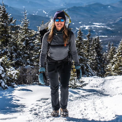 Person hiking in the snow with mountains and trees in the background