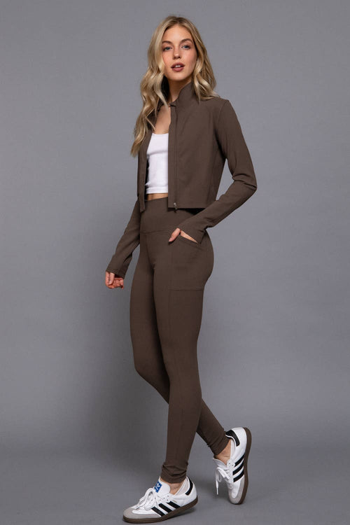 Woman wearing a brown outfit with a white top and Adidas shoes on a gray background