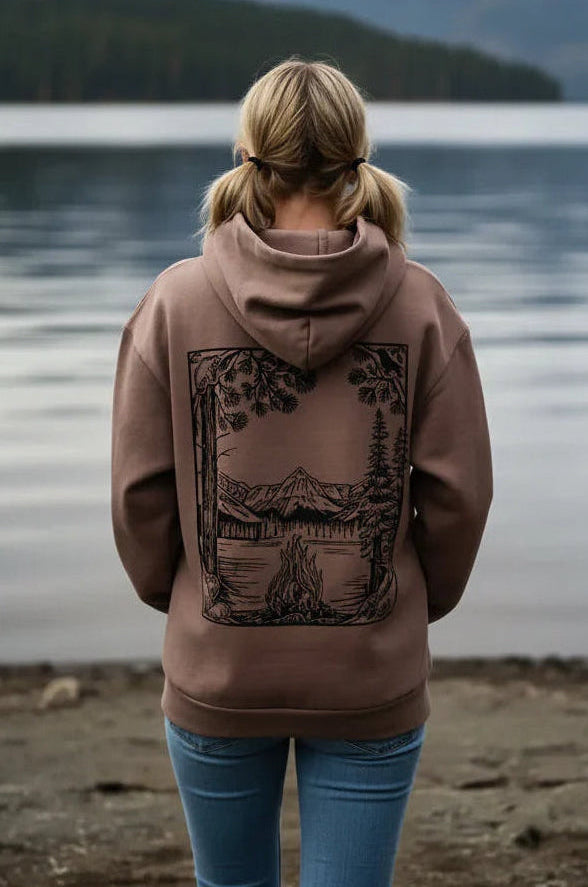Person wearing a brown hoodie with a nature-themed design, standing by a lake.