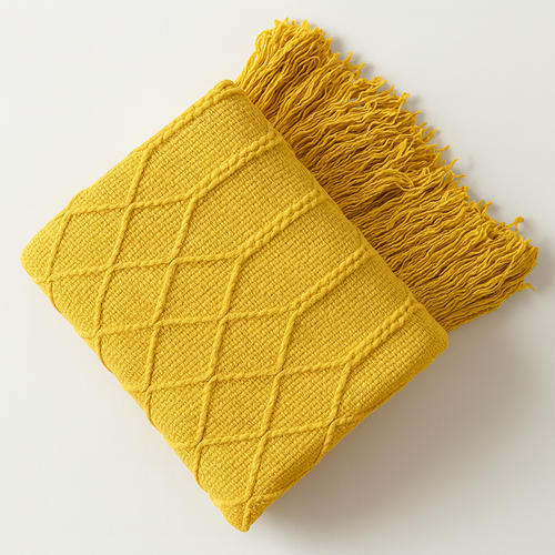 A folded mustard yellow knit throw blanket with a diamond cable pattern and fringed edges, shown on a clean white background.