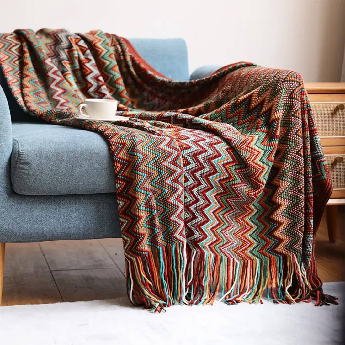 Colorful zigzag patterned blanket draped over a blue sofa with a cup on it, in a cozy living room setting.