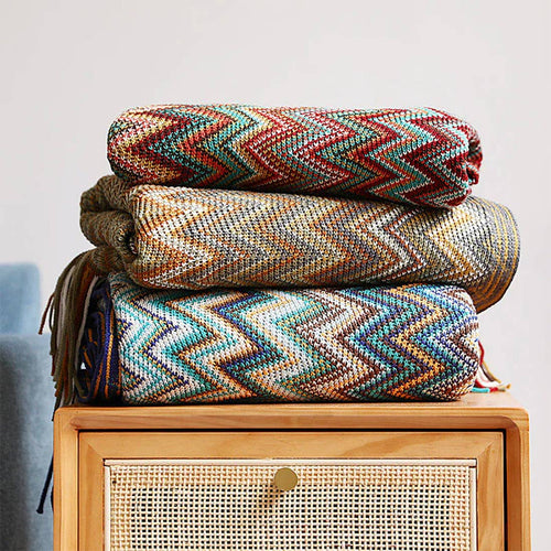 Stack of colorful woven blankets on a wooden cabinet with a light gray background