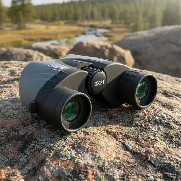 Crosman 8x21 binoculars on rocky terrain with forest and stream background