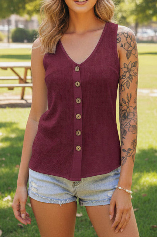 Woman wearing a maroon sleeveless button-up top and denim shorts outdoors.
