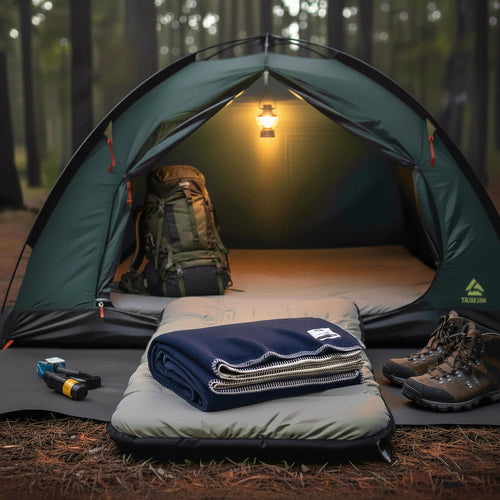 Camping scene with a tent, sleeping pad, and folded blanket in a forest setting.