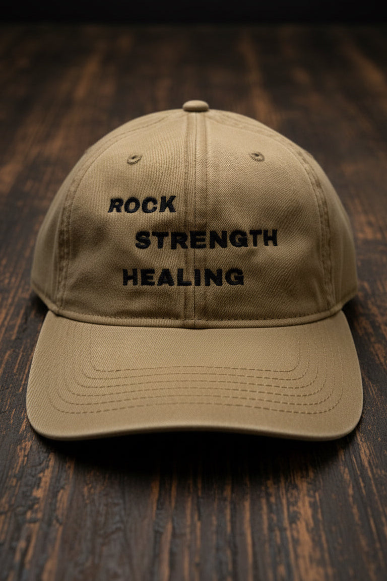 Beige cap with 'Rock Strength Healing' text on a wood floor