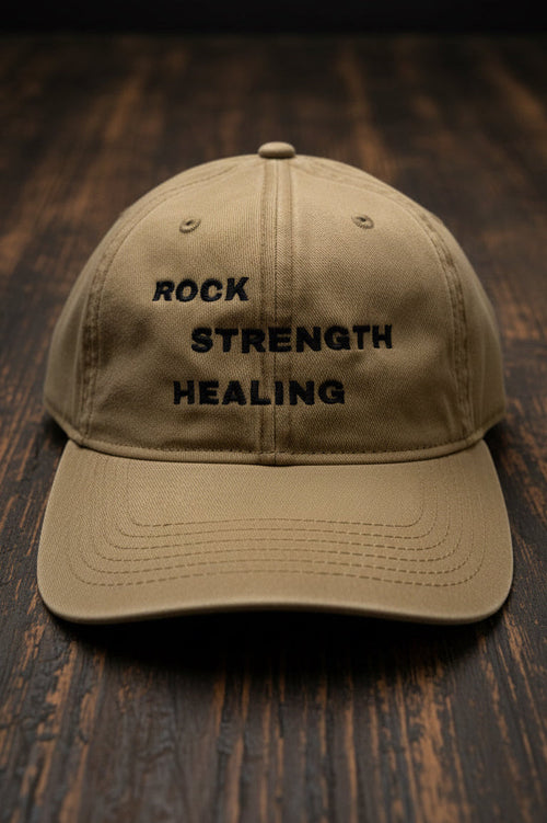 Beige cap with 'Rock Strength Healing' text on a wood floor