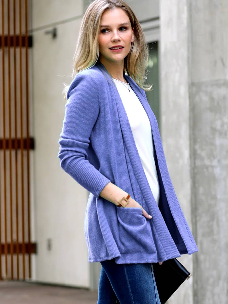 Woman wearing a long purple cardigan over a white top and blue jeans, standing outdoors.