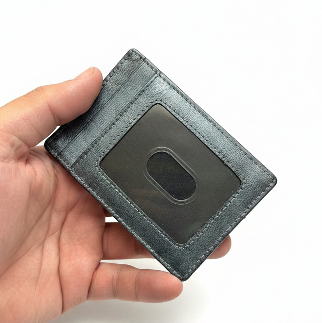 A dark gray leather card holder wallet with a clear ID window, held in a person's hand against a white background.
