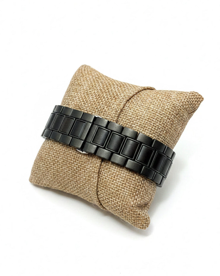 Black metal watch band on a textured beige pillow.