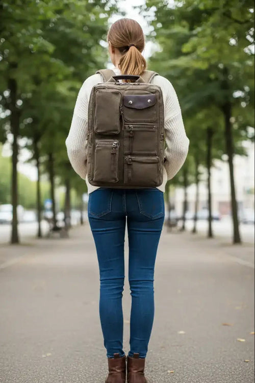 Woman walking away on tree-lined path wearing olive backpack, jeans, and boots