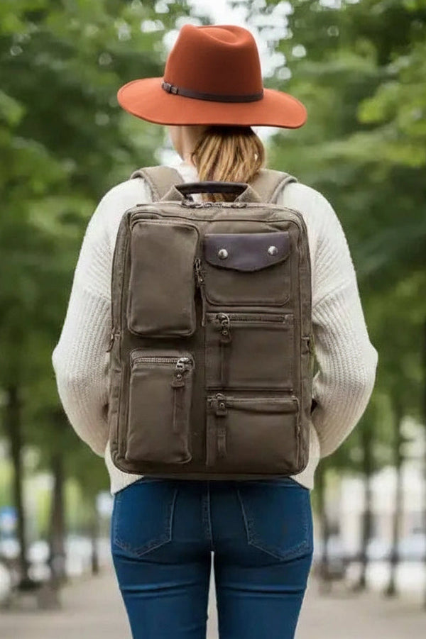 Woman walking away on tree-lined path wearing olive backpack, jeans, and boots