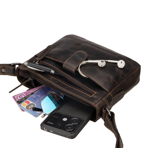 Brown leather crossbody bag with phone, cards, and earbuds on a white background