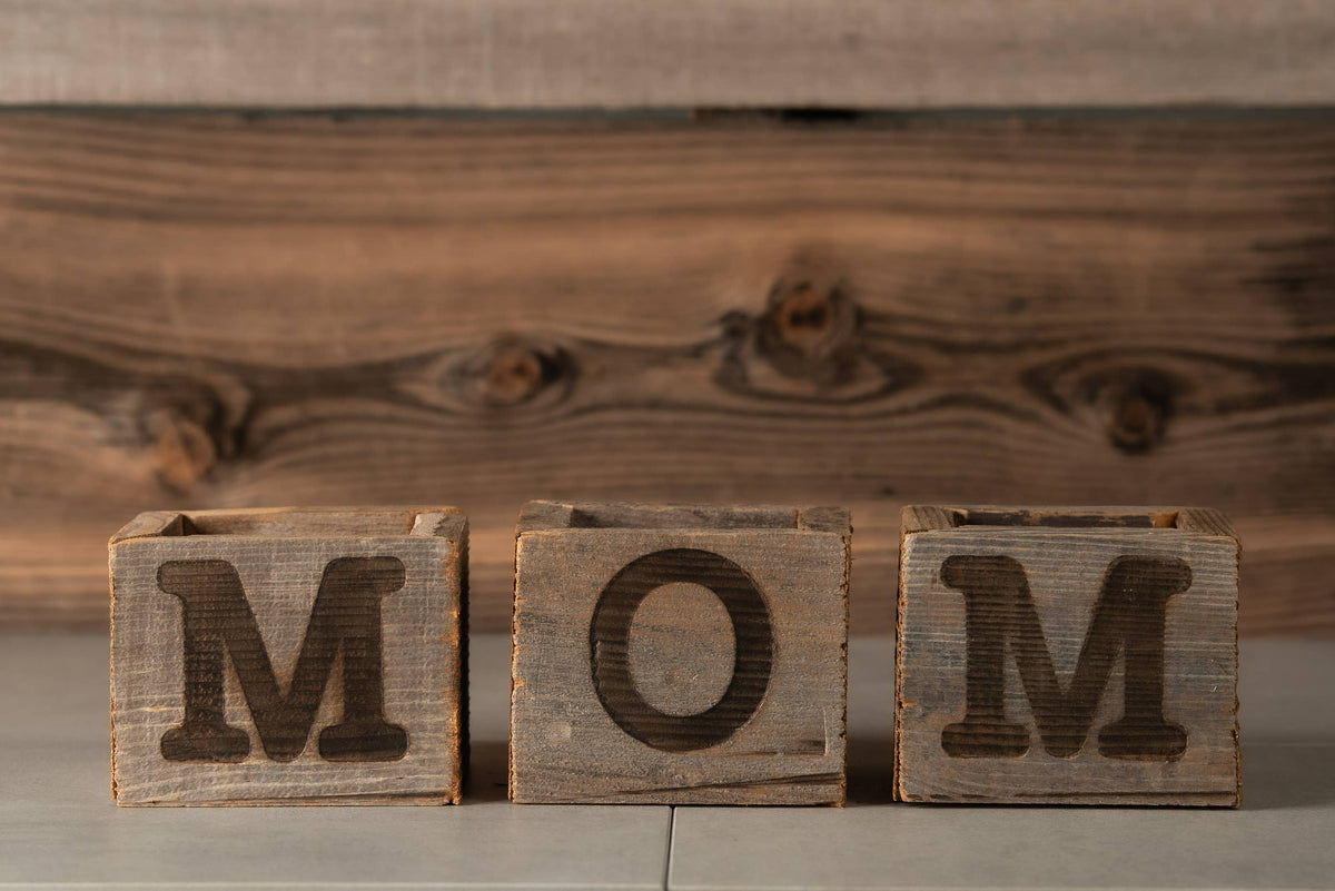 Wooden blocks with letters spelling 'MOM' against a wooden background