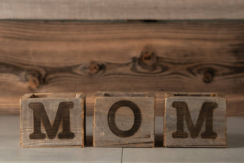 Wooden blocks with letters spelling 'MOM' against a wooden background