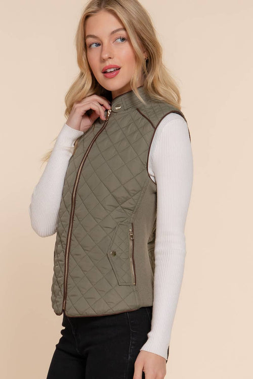 Woman wearing a quilted vest over a white long-sleeve shirt on a beige background