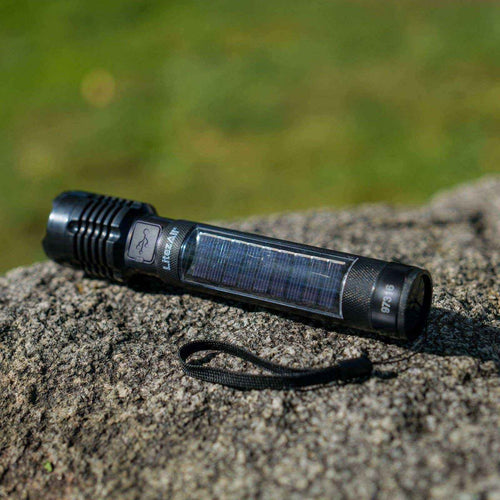 Black flashlight with solar panel on a rock with green grass in the background