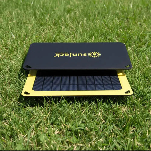 Portable SunJack solar charger on green grass, yellow frame, black panel with sun logo