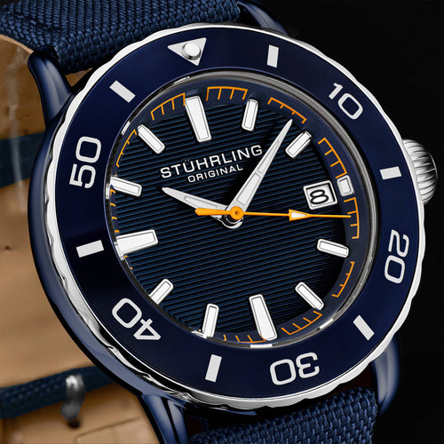 Stuhrling Original dive watch with a dark blue dial, matching blue bezel, white hour markers, and orange accents, paired with a blue fabric strap.