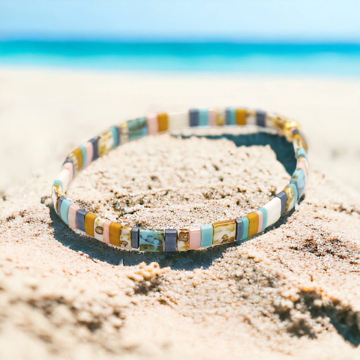 Colorful beaded bracelet on a sandy beach with a clear blue sky.