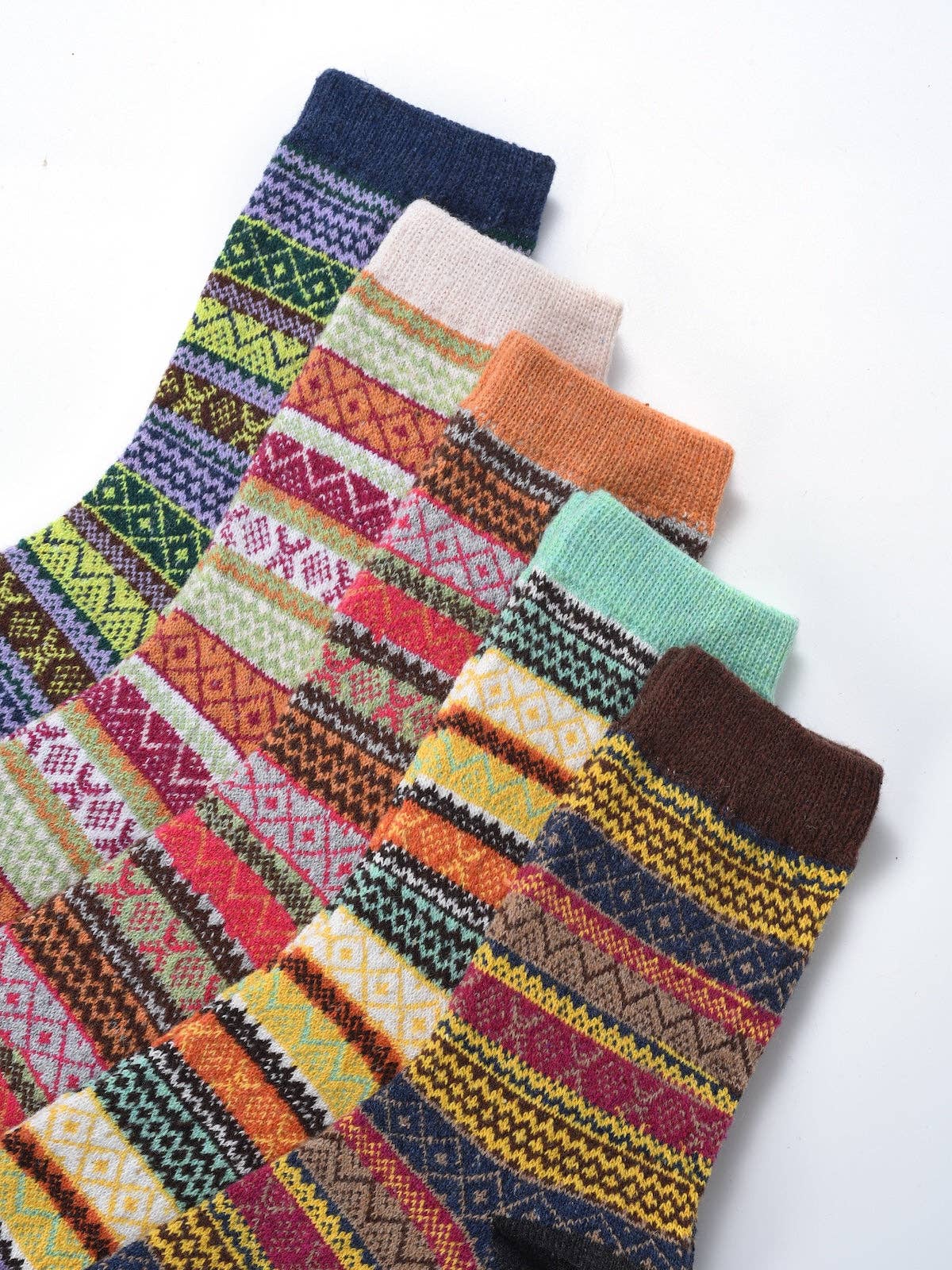Six pairs of patterned crew socks arranged diagonally on a white background, showcasing various colorful Fair Isle and geometric stripe designs.