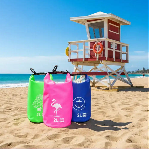 Three colorful 2L waterproof bags with turtle, flamingo, and anchor designs on sandy beach near lifeguard tower