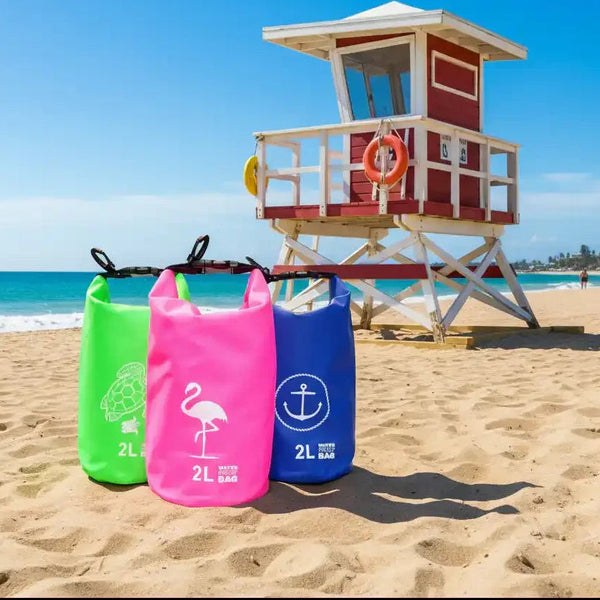 Three colorful 2L waterproof bags with turtle, flamingo, and anchor designs on sandy beach near lifeguard tower