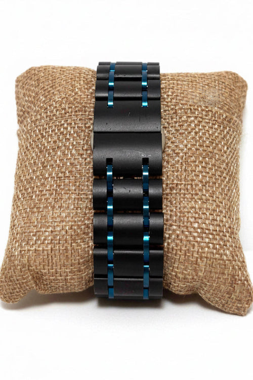 Wood Watch Pilot Black metal bracelet with blue accents on a textured brown surface